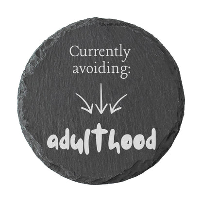 Round slate coaster with humorous text 'Currently avoiding: adulthood' on a white background