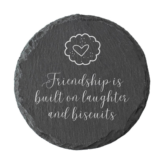 Round slate coaster with a heart and text reading "Friendship is built on laughter and biscuits" on a white background