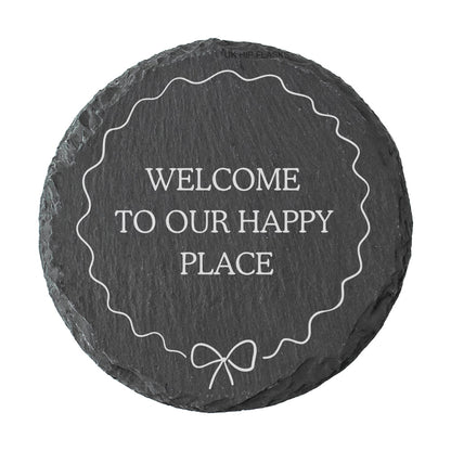Round slate coaster with 'Welcome to our happy place' text on a white background