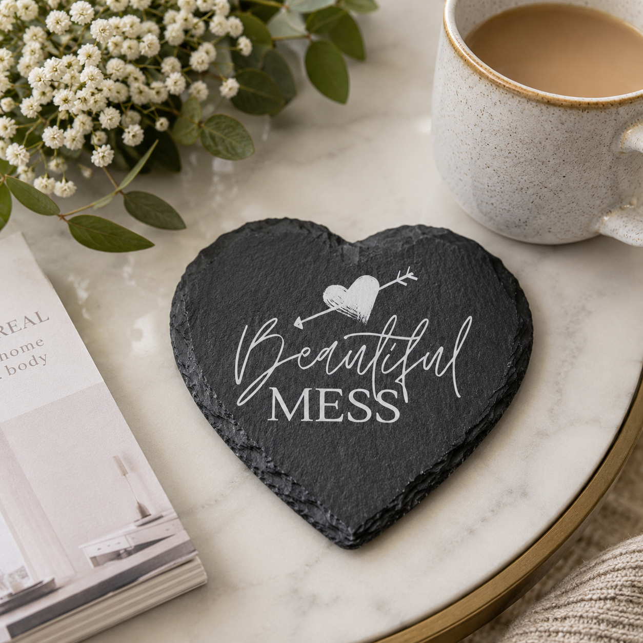 Heart-shaped slate coaster with 'Beautiful Mess' text on a marble surface with a cup of coffee and flowers.