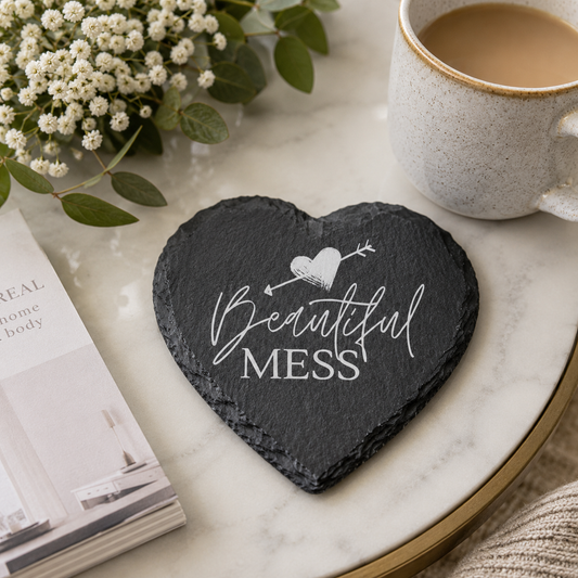 Heart-shaped slate coaster with 'Beautiful Mess' text on a marble surface with a cup of coffee and flowers.