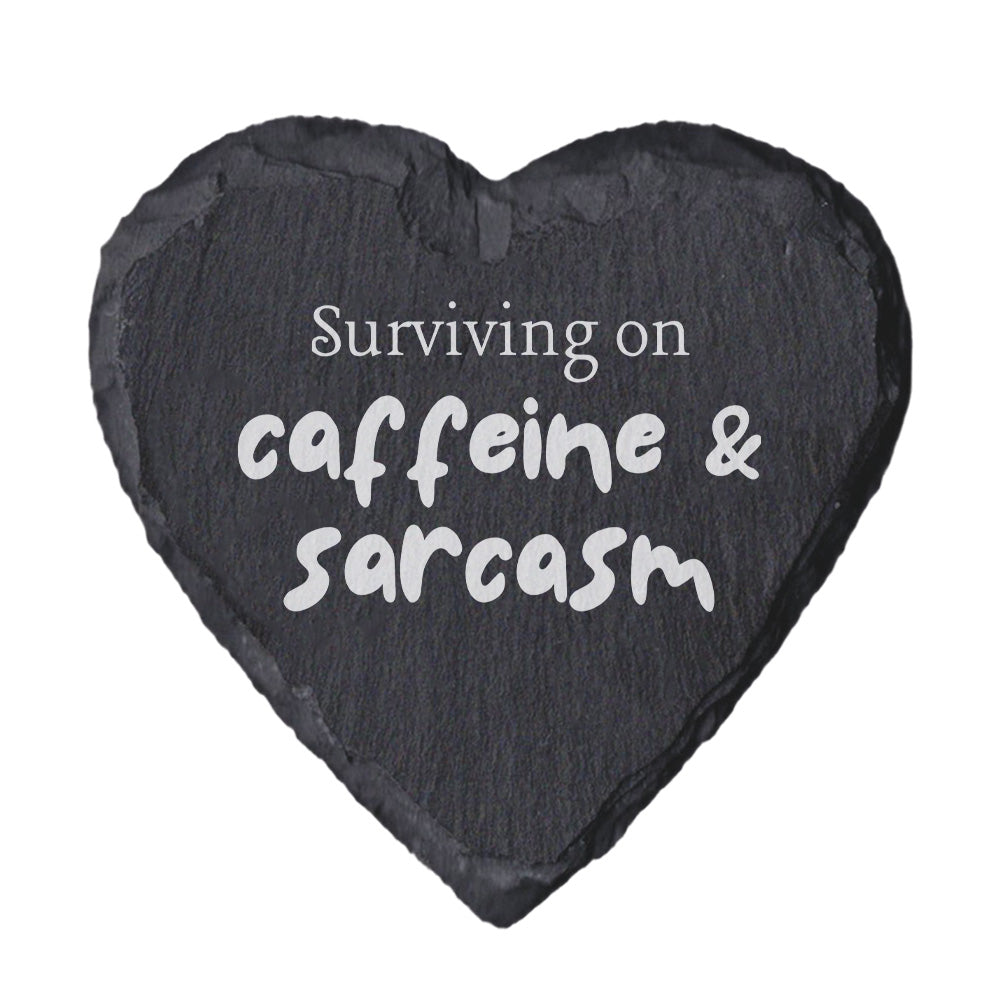 Heart-shaped slate coaster with text 'Surviving on caffeine & sarcasm' on a white background