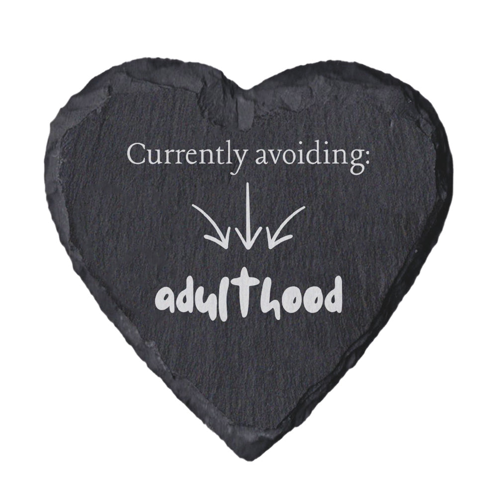 Heart-shaped slate coaster with text 'Currently avoiding: adulthood' on a white background