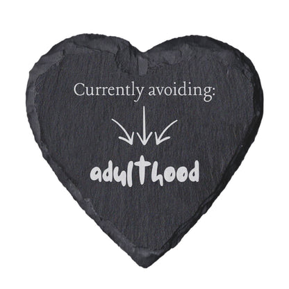 Heart-shaped slate coaster with text 'Currently avoiding: adulthood' on a white background