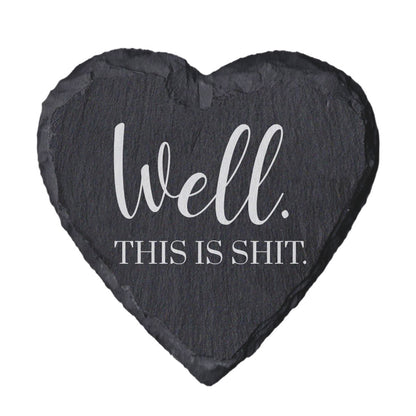 Heart-shaped slate coaster with text 'Well. This is shit.' on a white background