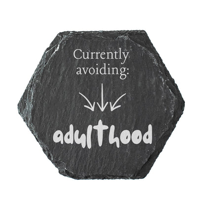 Hexagonal black slate coasters with white text 'Currently avoiding: adulthood'