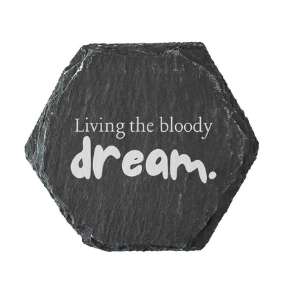Hexagonal black slate coaster with 'Living the bloody dream.' text on a white background