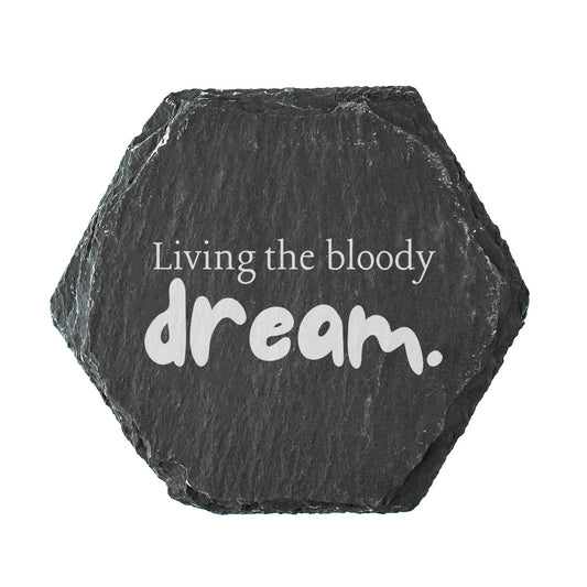 Hexagonal black slate coaster with 'Living the bloody dream.' text on a white background