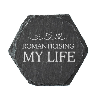 Hexagonal black slate coaster with 'ROMANTICISING MY LIFE' text on a white background