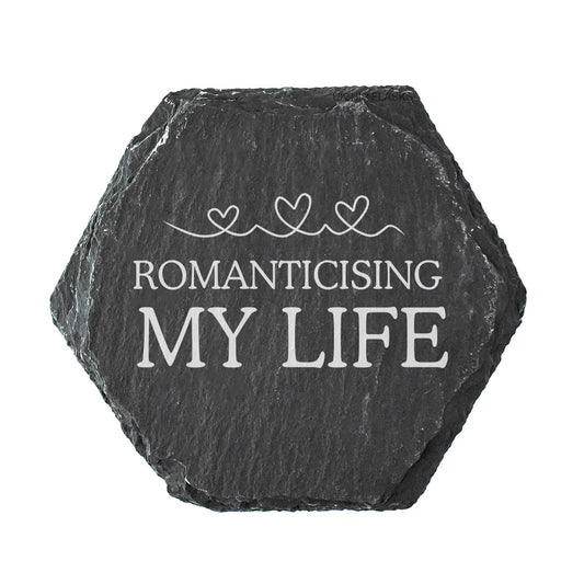 Hexagonal black slate coaster with 'ROMANTICISING MY LIFE' text on a white background