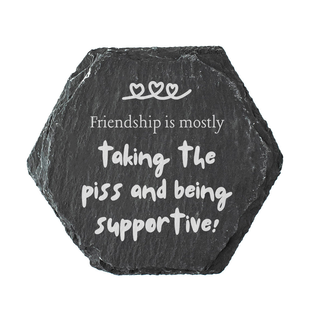 Hexagonal black slate coaster with white text 'Friendship is mostly taking the piss and being supportive!' on a white background