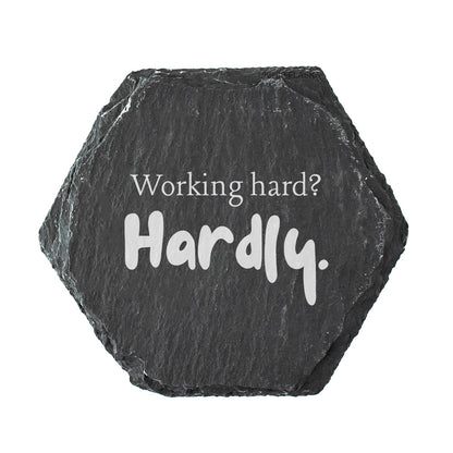 Hexagonal black slate coaster with 'Working hard? Hardly.' text on a white background