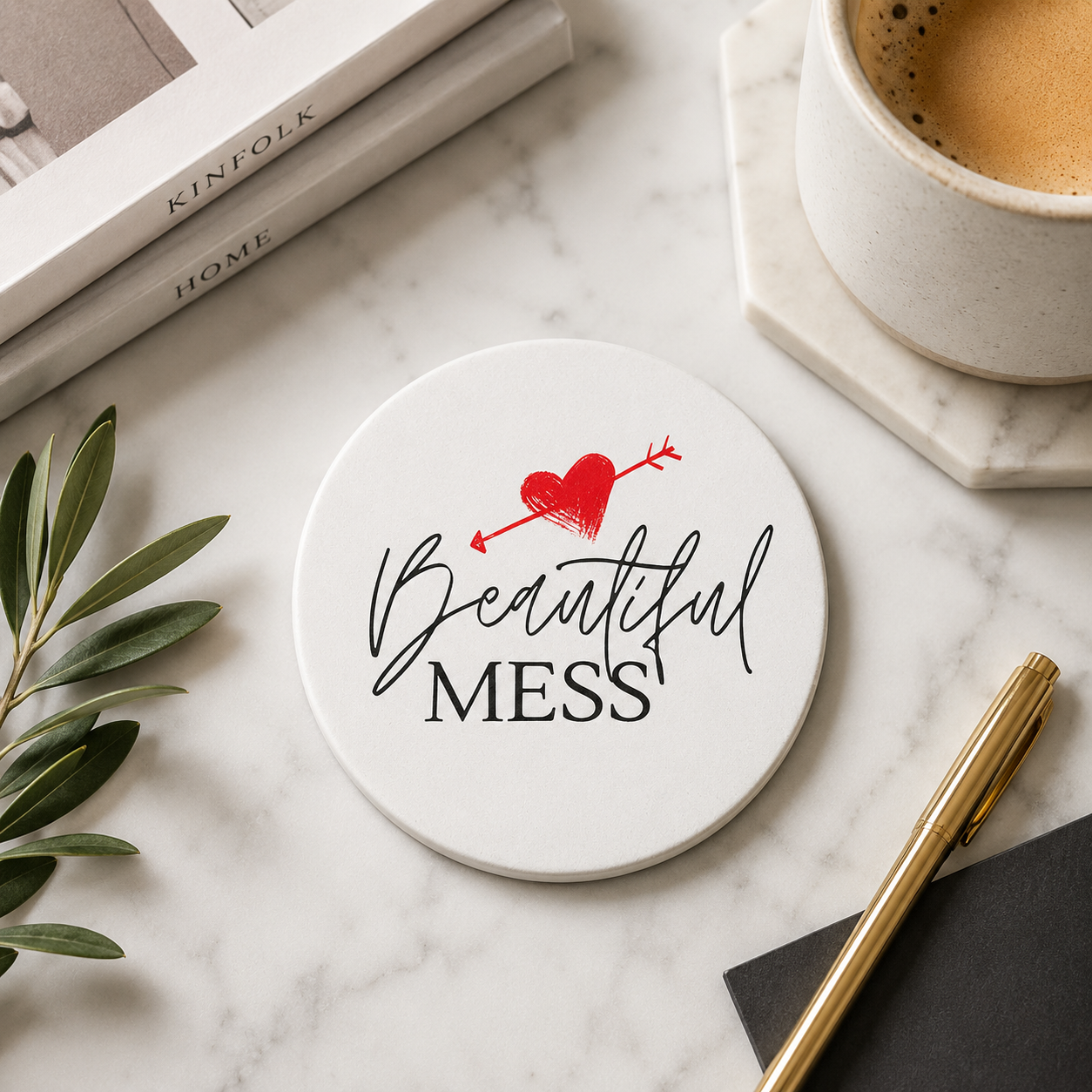 Round ceramic coaster with the quote "Beautiful Mess" in black and red text. The coaster is on a marble surface with books and a coffee.