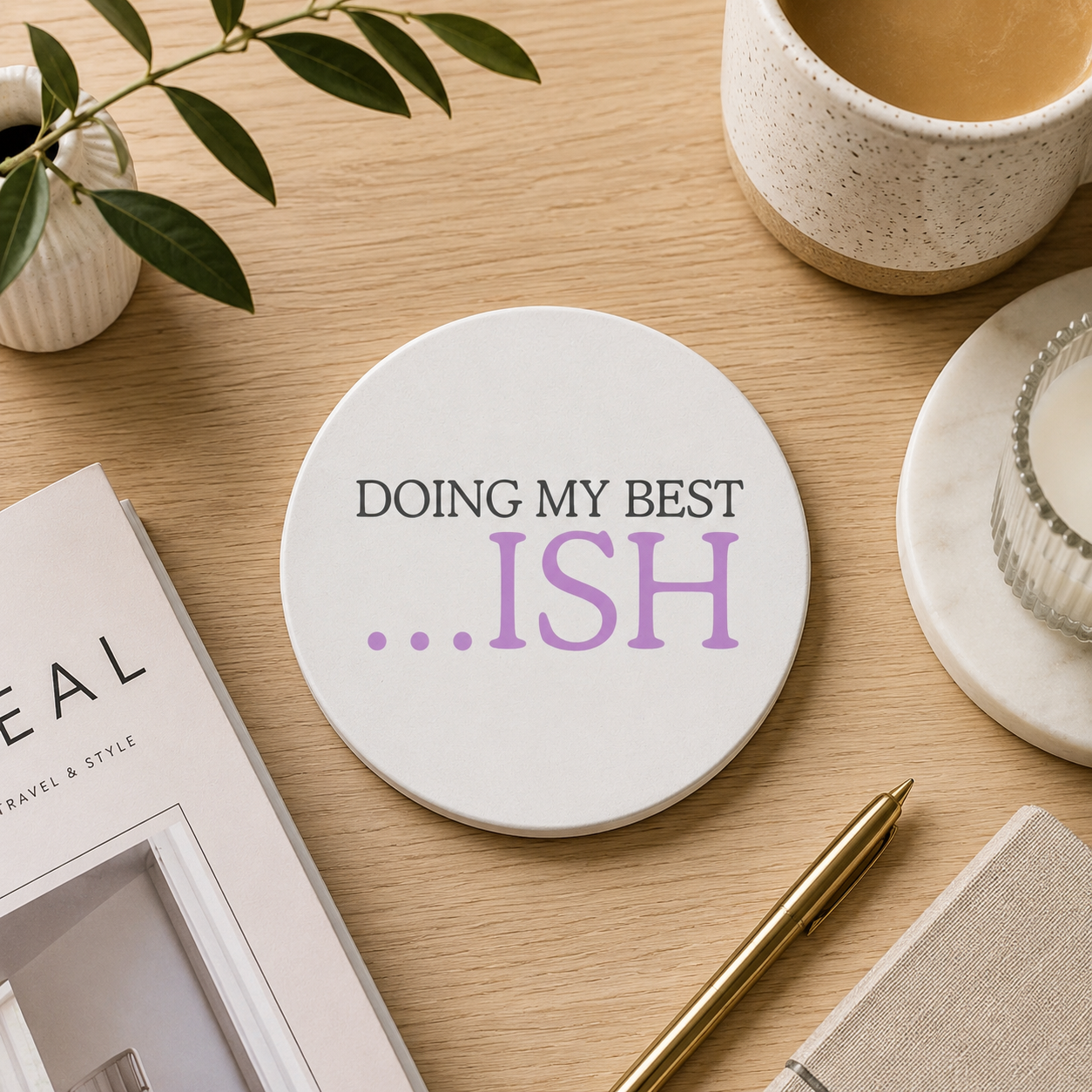 A round white ceramic coaster with the quote 'Doing my best... ISH' in grey and purple text. The coaster is set on a wooden desk with tea and stationery.