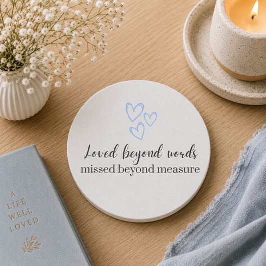 Round ceramic coaster featuring the thoughtful words "Loved beyond words, missed beyond measure". The coaster is on a wooden surface with a candle.
