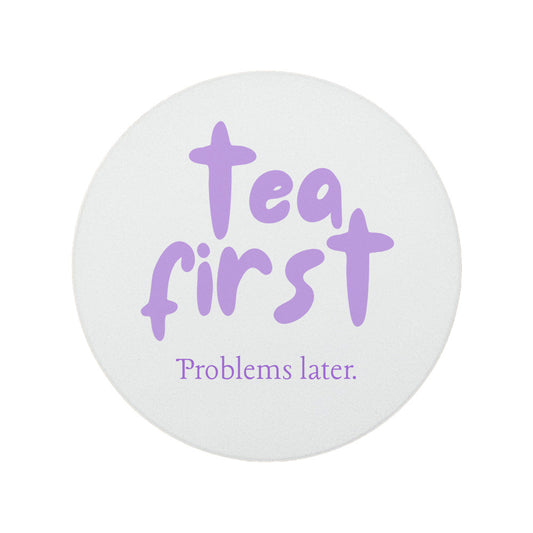 Round ceramic coaster featuring the humorous sarcastic quote "Tea first, problems later." in crisp purple lettering. 