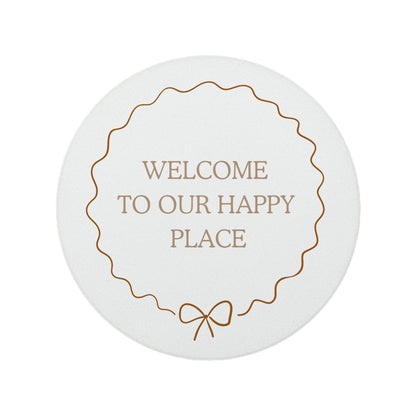 Round ceramic coaster featuring the quote "Welcome to our happy place" in neutral toned lettering with a cute bow border.