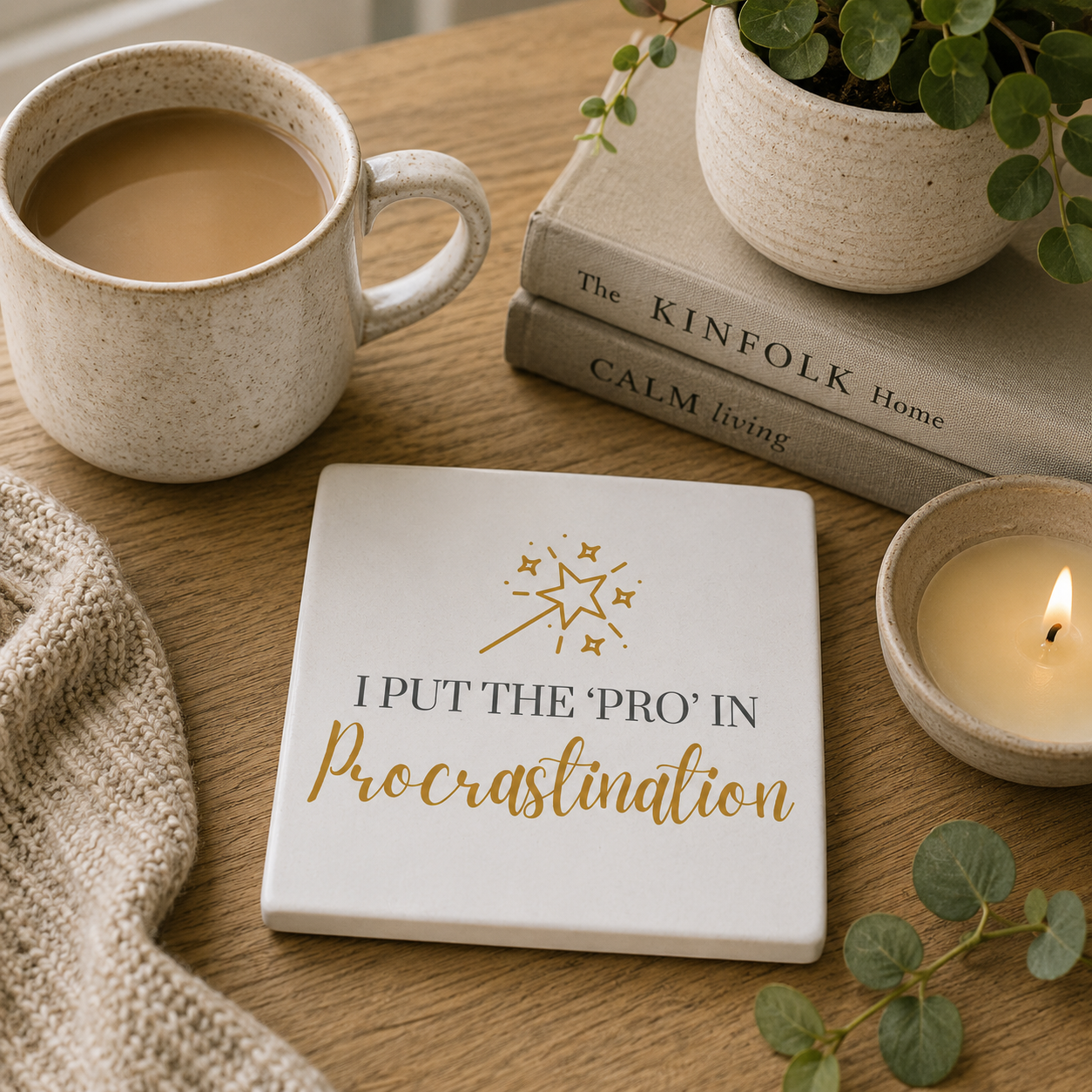 Square ceramic coaster featuring the funny quote "I put the 'pro' in procrastination" in crisp black and gold lettering with a magic wand and stars illustration, on a wooden surface with tea cup and books.