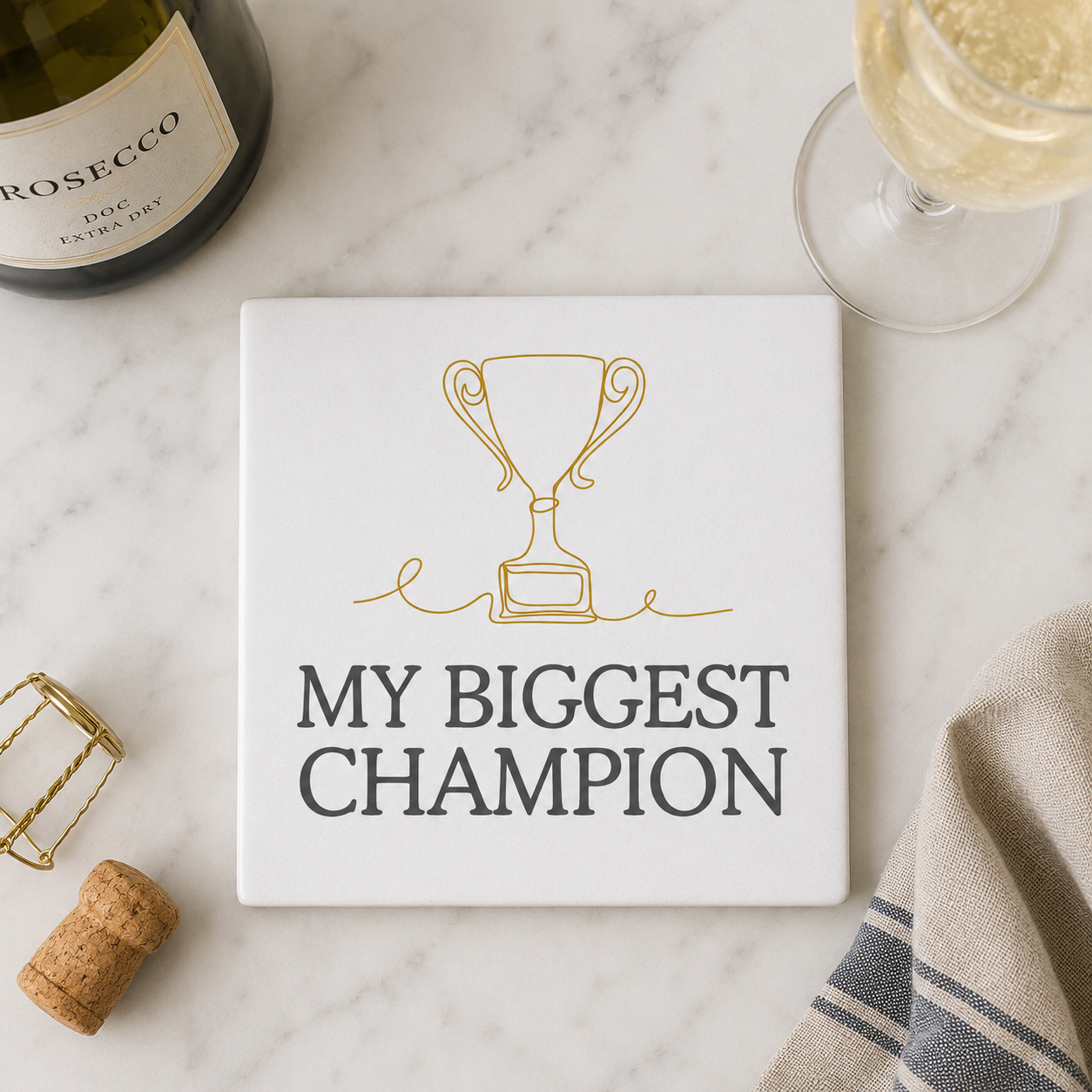 Square ceramic coaster with 'My Biggest Champion' design on a marble surface with wine bottle and glass.