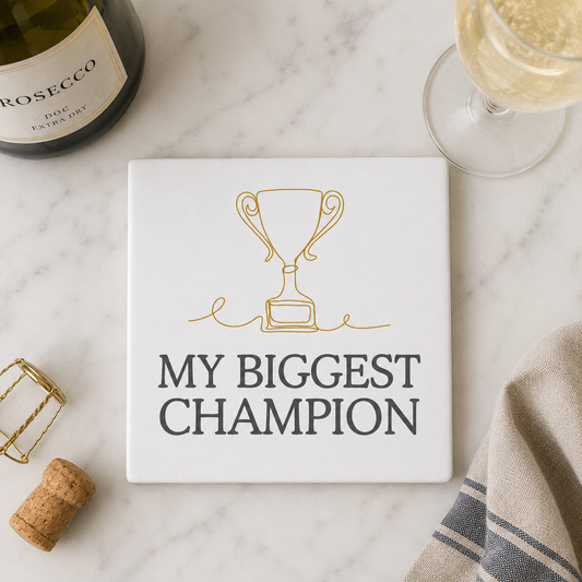 Square ceramic coaster with 'My Biggest Champion' design on a marble surface with wine bottle and glass.