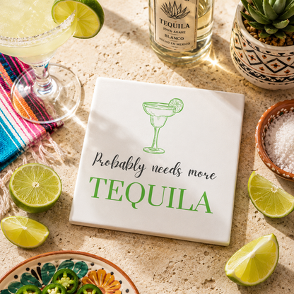 Square ceramic coaster featuring the funny quote "Probably needs more tequila" in crisp grey and green lettering with a margarita glass illustration, on a stone surface with tequila bottle and margarita cocktails.