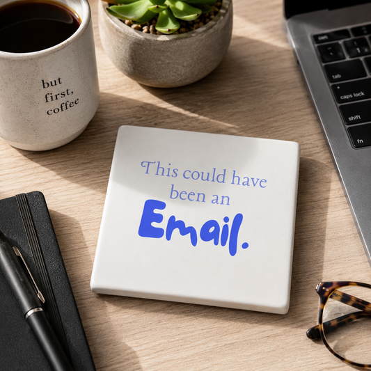 Square ceramic coaster featuring the humorous sarcastic quote "This could have been an email" in blue lettering, on a desk with laptop, notebook and pen.