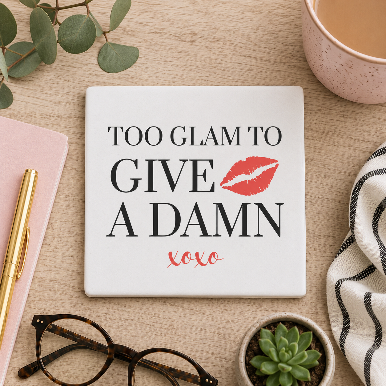 Square ceramic coaster featuring the witty quote "Too glam to give a damn" in grey text with a red illustrated lipstick print, on a wooden surface with cup of tea and glasses.