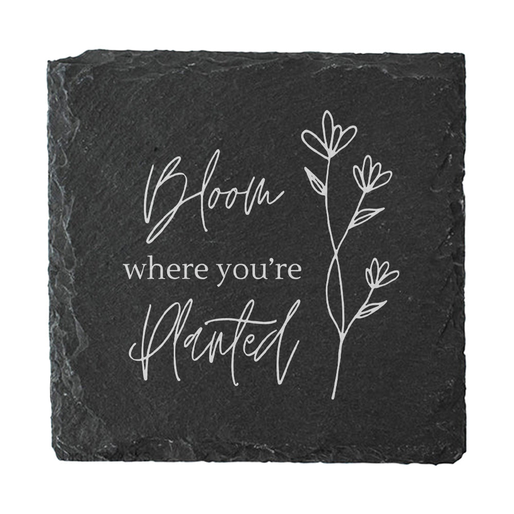 Black slate coaster with 'Bloom where you're planted' text and floral design on a white background