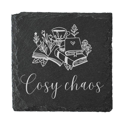 Black slate coaster with white illustrations of books and flowers, and the text 'Cosy chaos'.