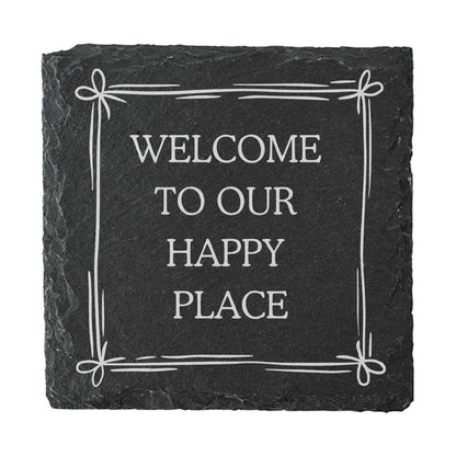 A slate coaster with the quote "Welcome to our happy place" in white text.