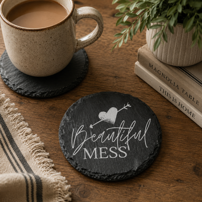 Round slate coaster with 'Beautiful Mess' text on a wooden table with cup of tea and books.
