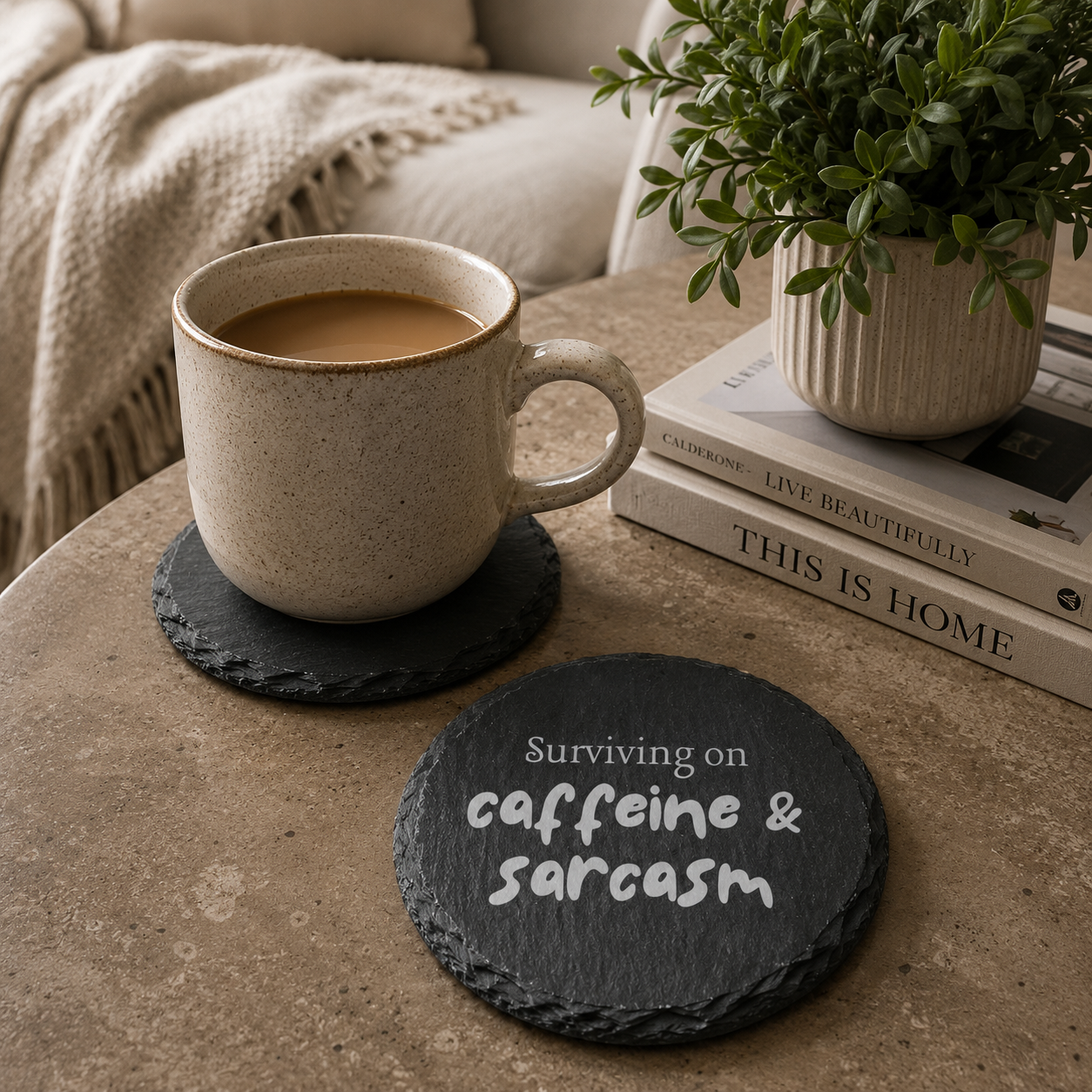 Round slate coaster with 'surviving on caffeine and sarcasm' text, placed on a table with a plant and books in the background.