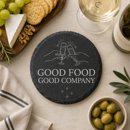 Round slate coaster with 'Good Food Good Company' text on a table with food and wine.