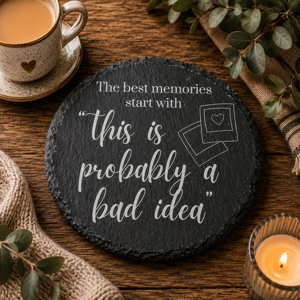Round slate coaster with humorous quote on a wooden table with a cup of coffee and candle.