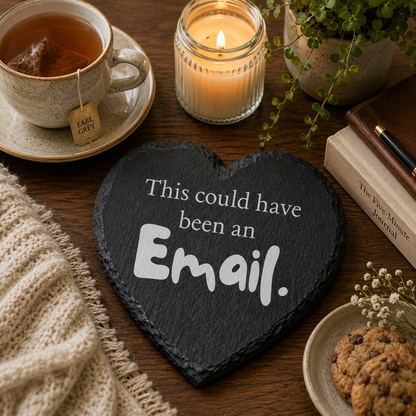 Heart-shaped slate coaster with text 'This could have been an Email.' on a table with tea, cookies, and a candle.
