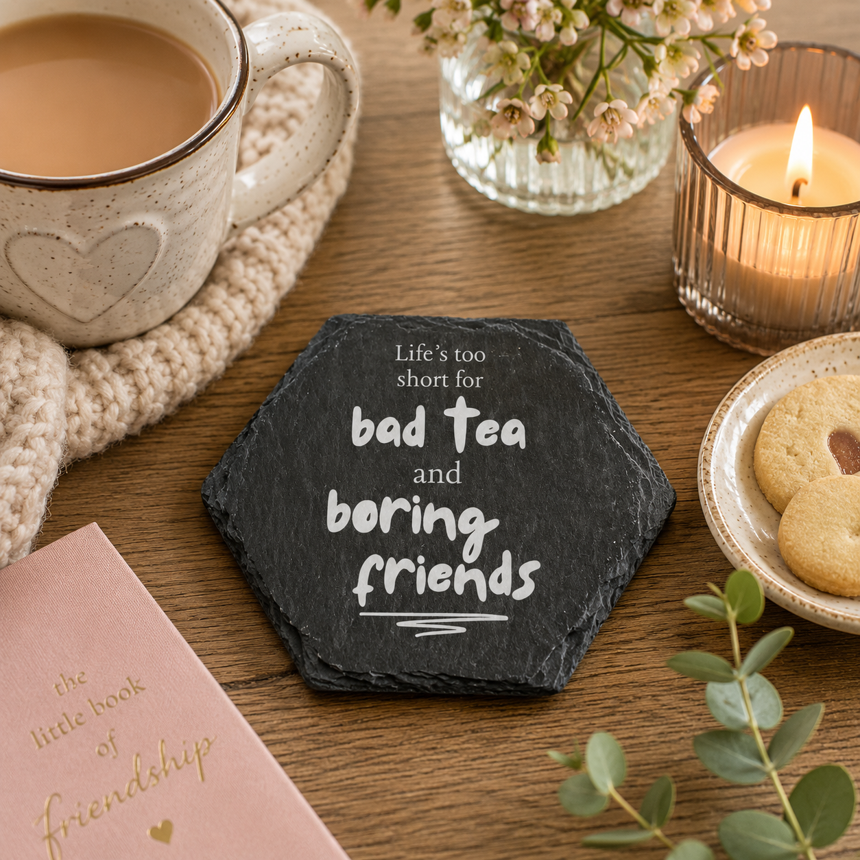 Hexagonal slate coaster with 'Life's too short for bad tea and boring friends' text on a wooden surface with plants, tea and books.