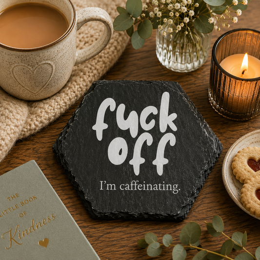 Hexagonal slate coaster with 'fuck off I'm caffeinating' text on a wooden surface with plants.