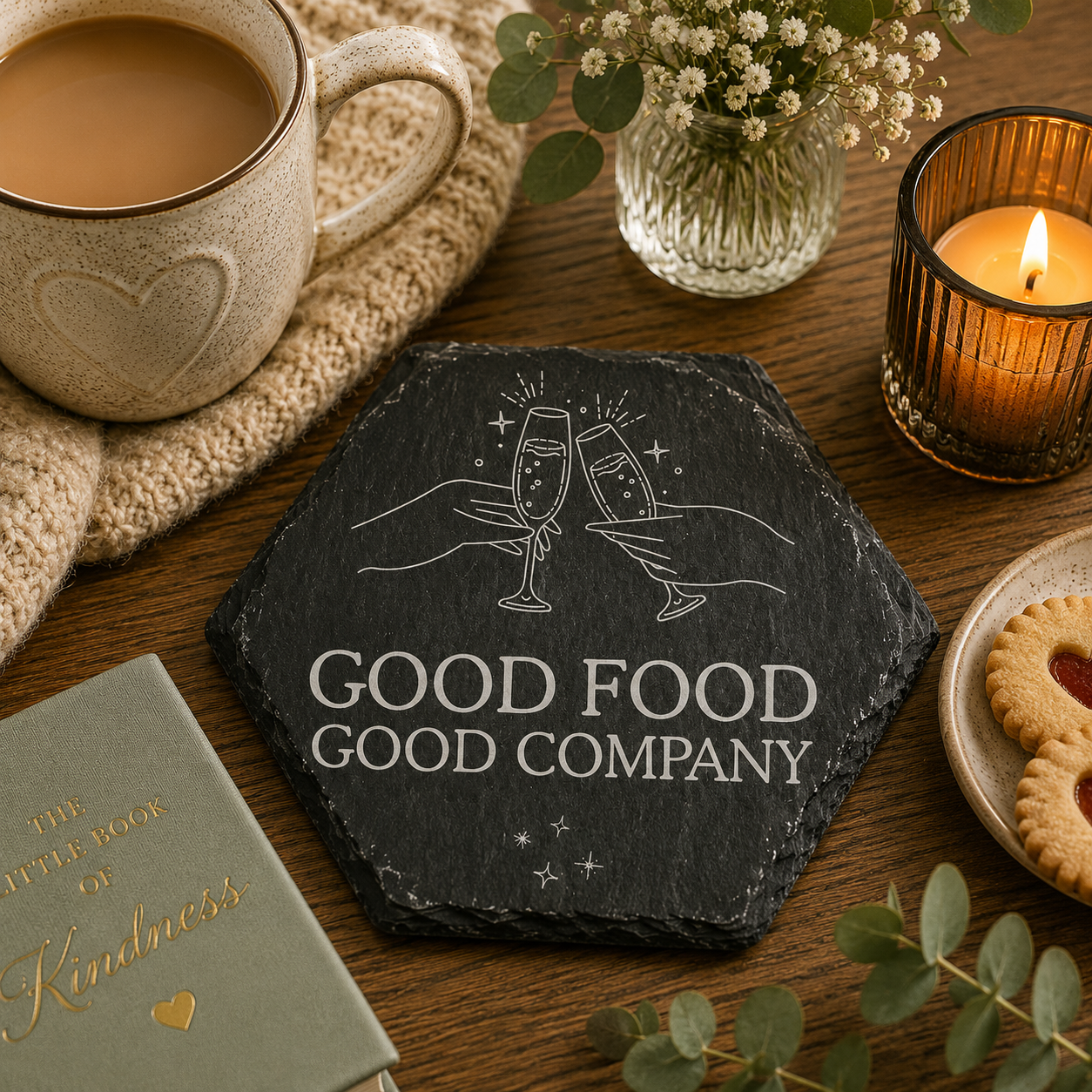 Hexagonal slate coaster with 'good food good company' text on a wooden surface with plants, tea and candles.