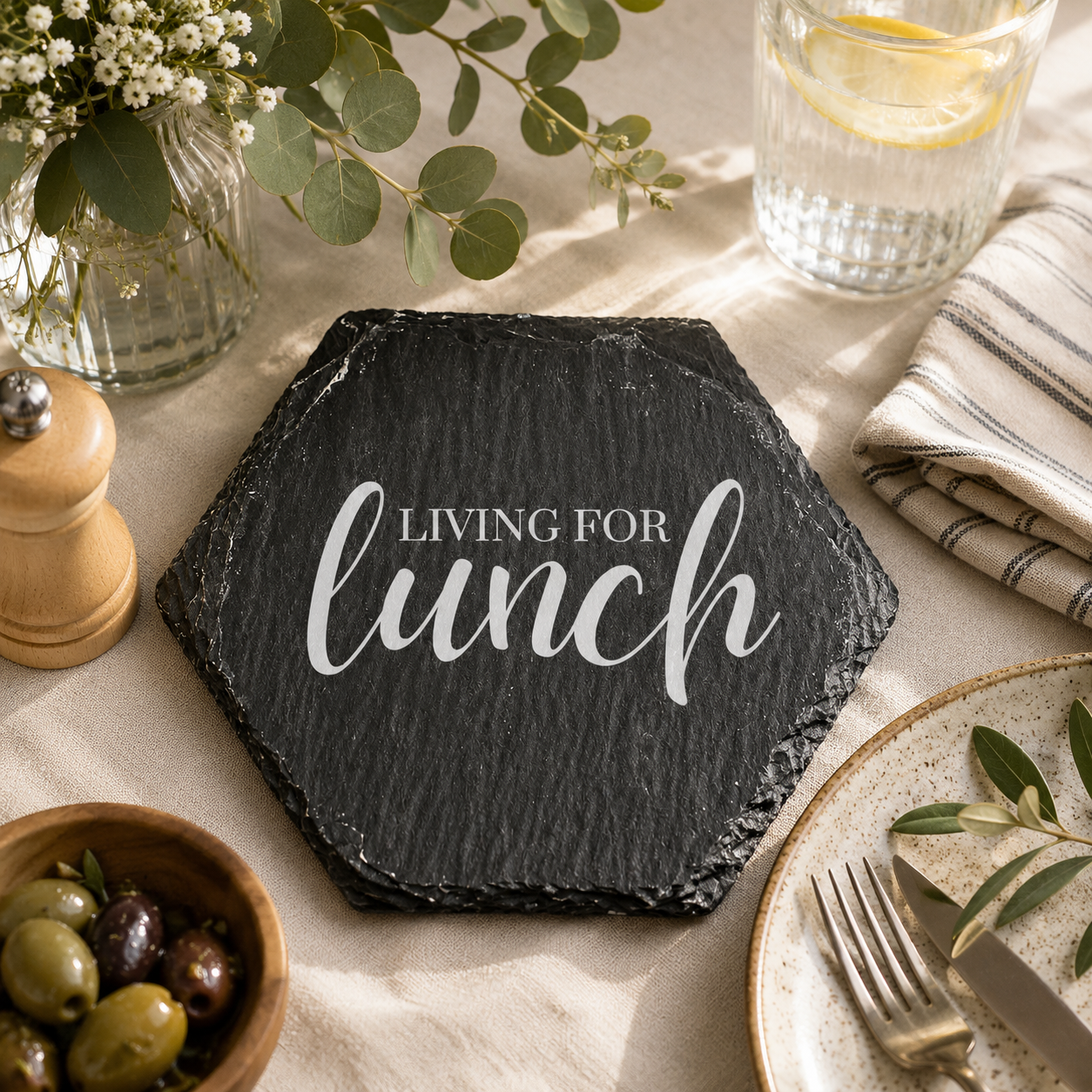 Hexagonal slate coaster with 'living for lunch' text on a wooden surface with plants.