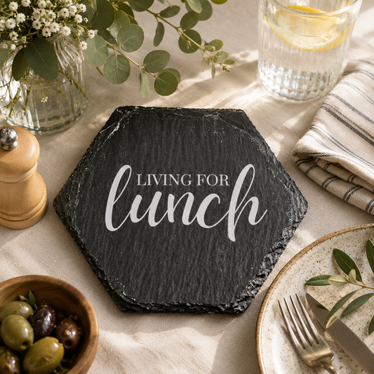 Hexagonal slate coaster with 'living for lunch' text on a wooden surface with plants.