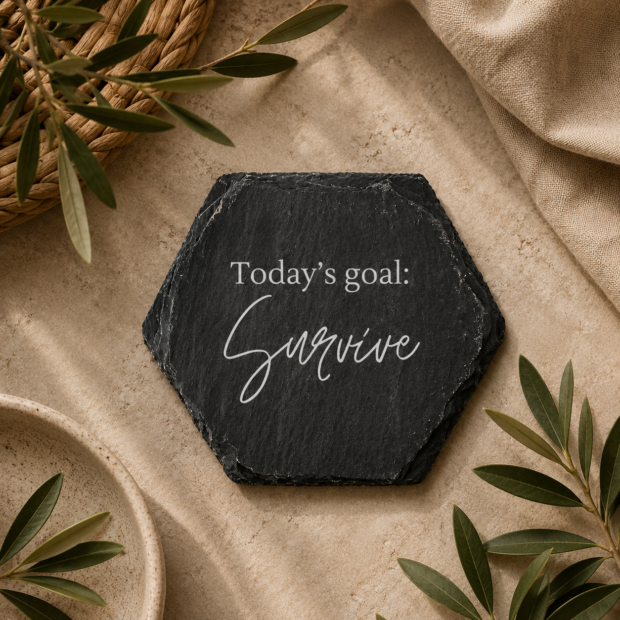 Hexagonal slate coaster with 'today's goal: survive' text on a wooden surface with plants.