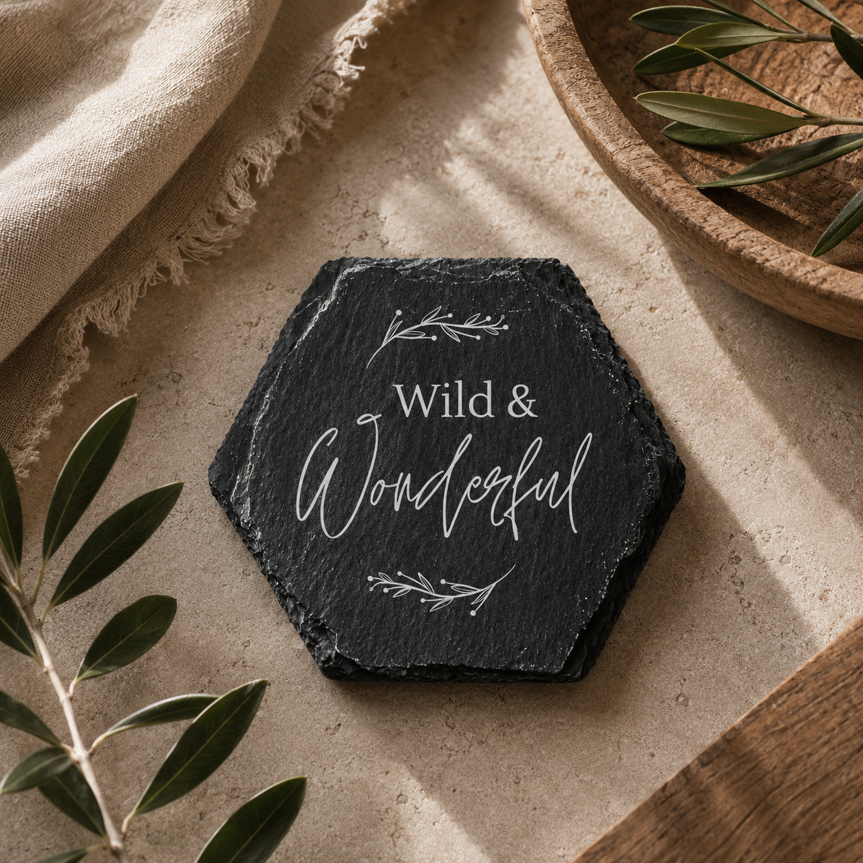 Hexagonal slate coaster with 'Wild & Wonderful' text on a neutral background with leaves.