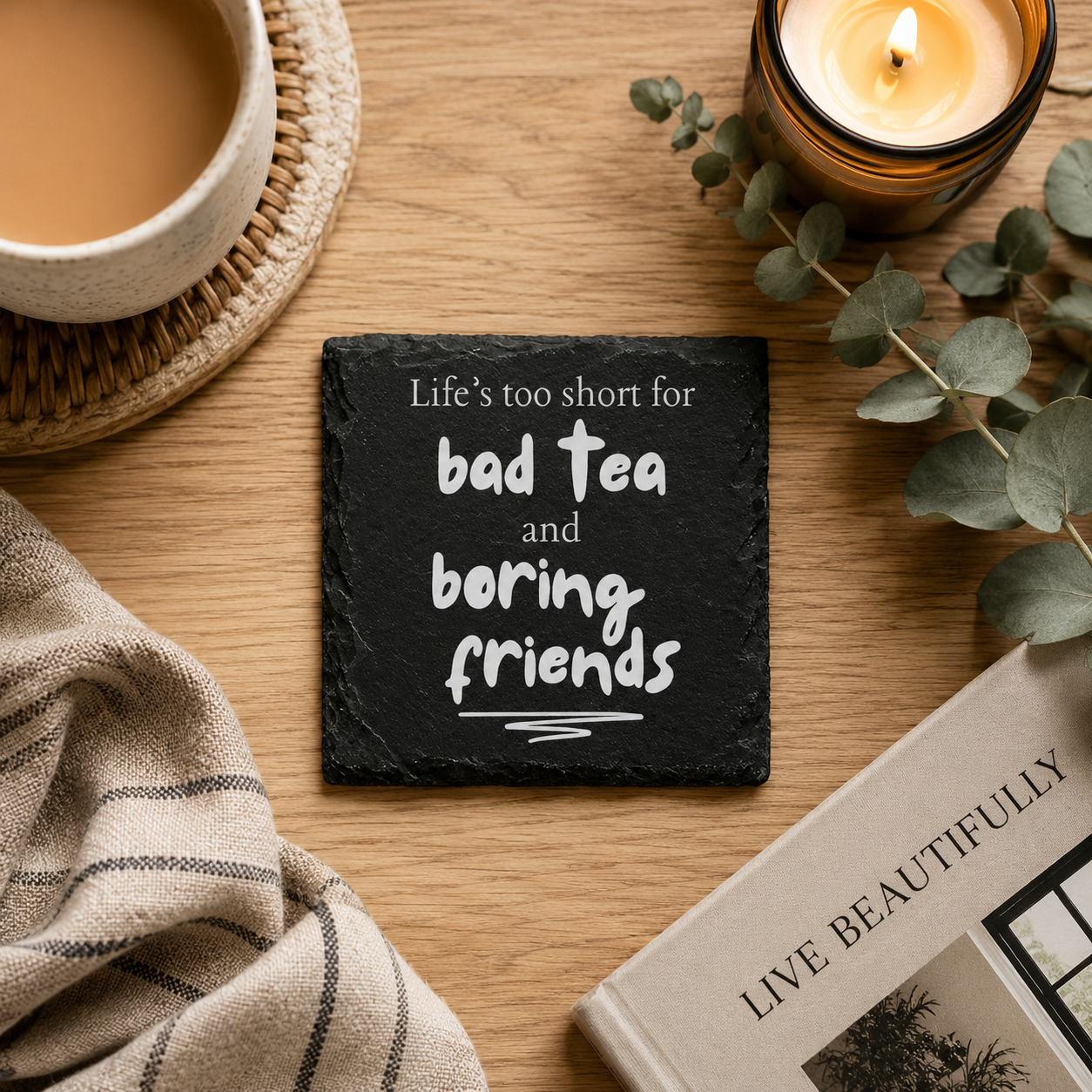 Square slate coaster with the quote "Life's too short for bad tea and boring friends!" on a wooden table with books and a cup of tea.