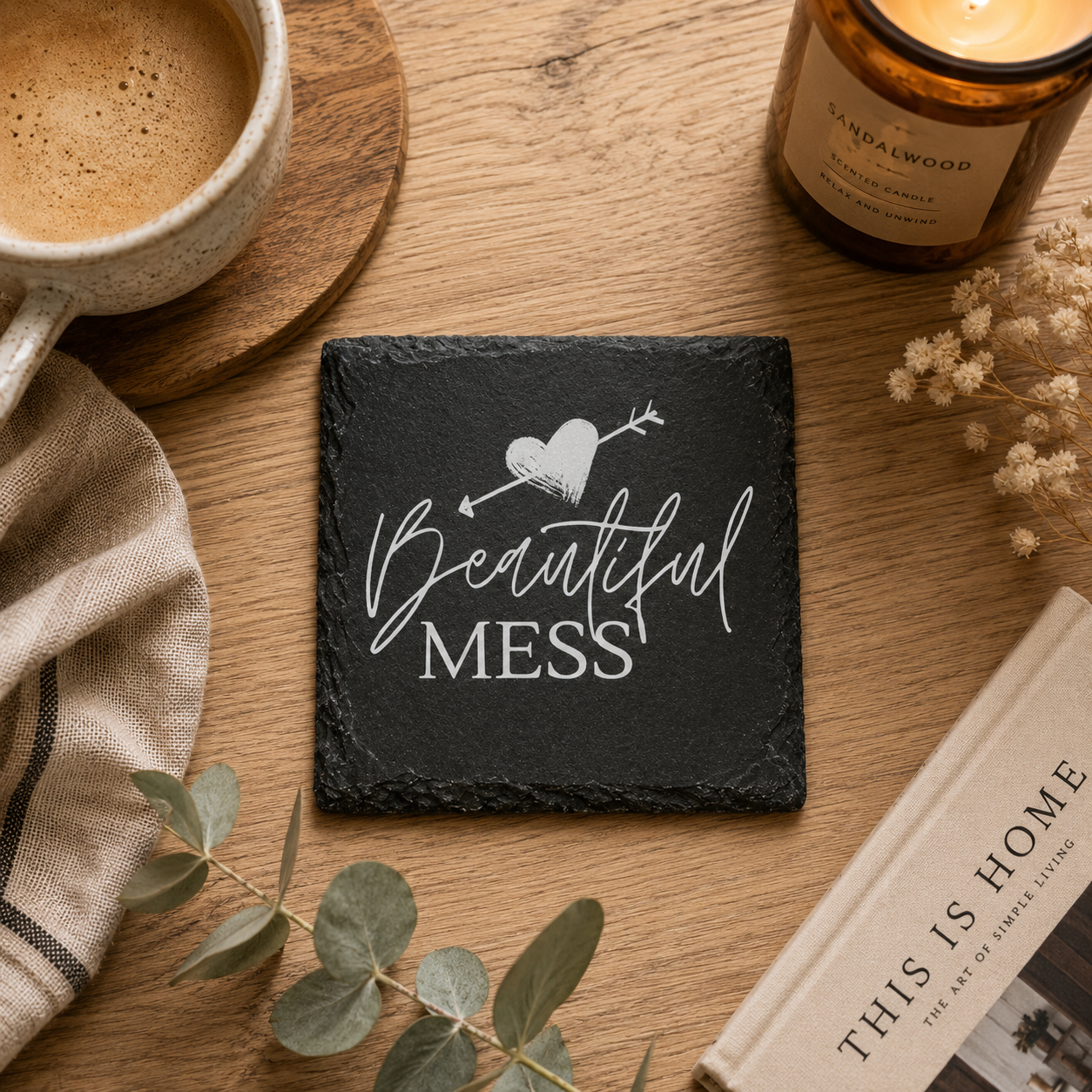 Slate coaster with 'Beautiful Mess' design on a wooden table with coffee, candle, and book.