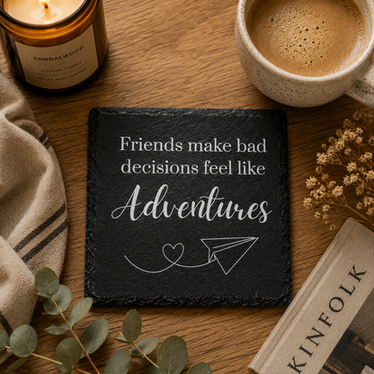Slate coaster with motivational quote, mug of coffee, candle, and book on wooden surface