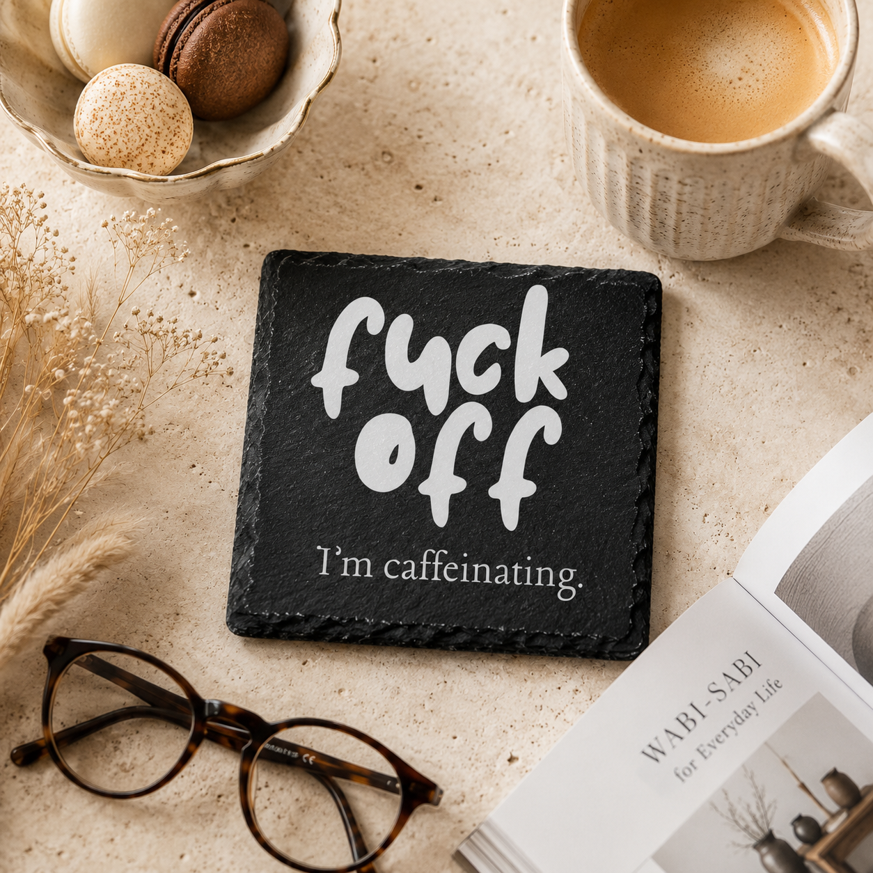 Slate coaster with 'fuck off, I'm caffeinating' text on a table with coffee and glasses.