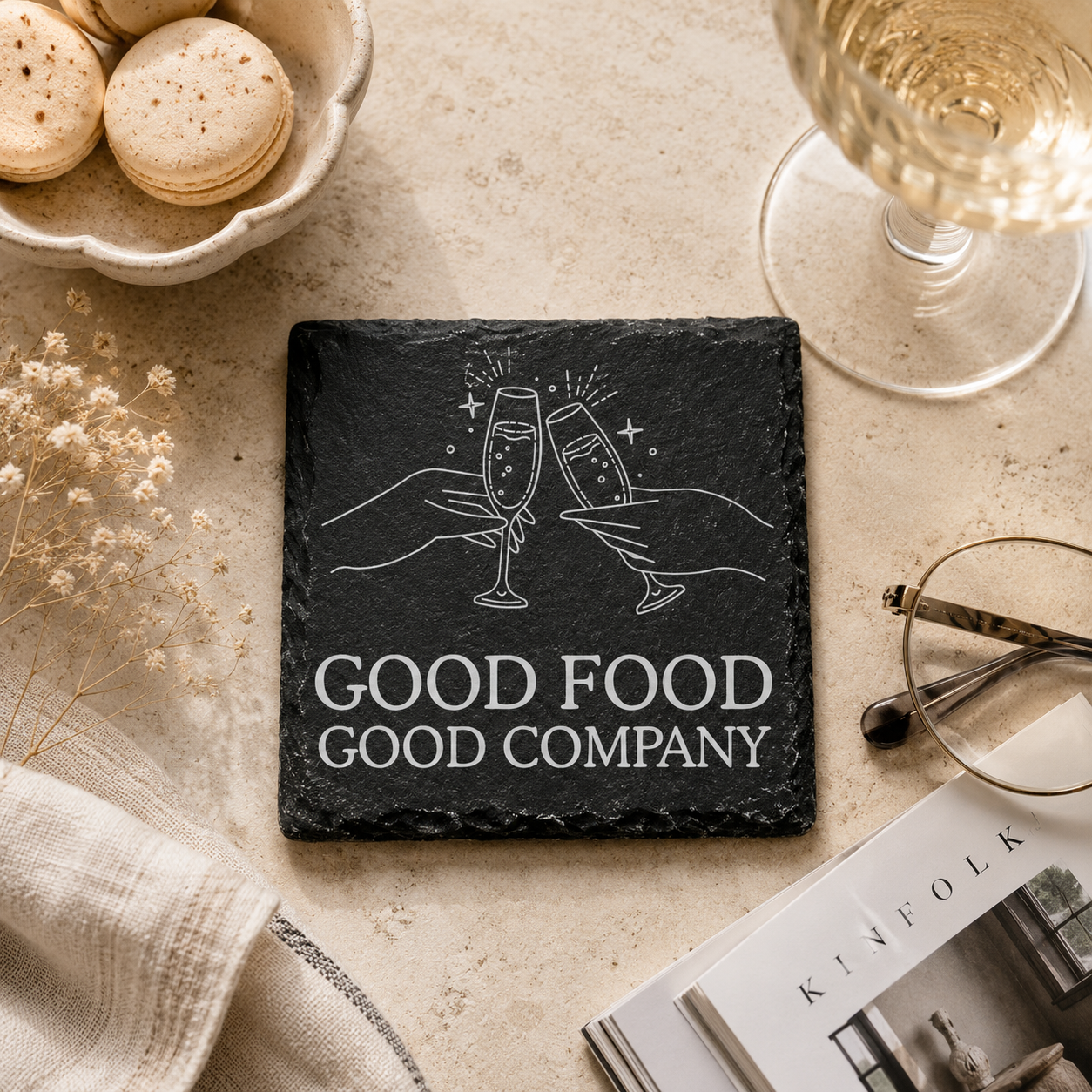 Slate coaster with 'Good Food Good Company' text and champagne glasses on a table with macarons and a glass of wine.