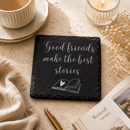 Slate coaster with 'Good friends make the best stories' quote on a cozy setting with a candle and book.