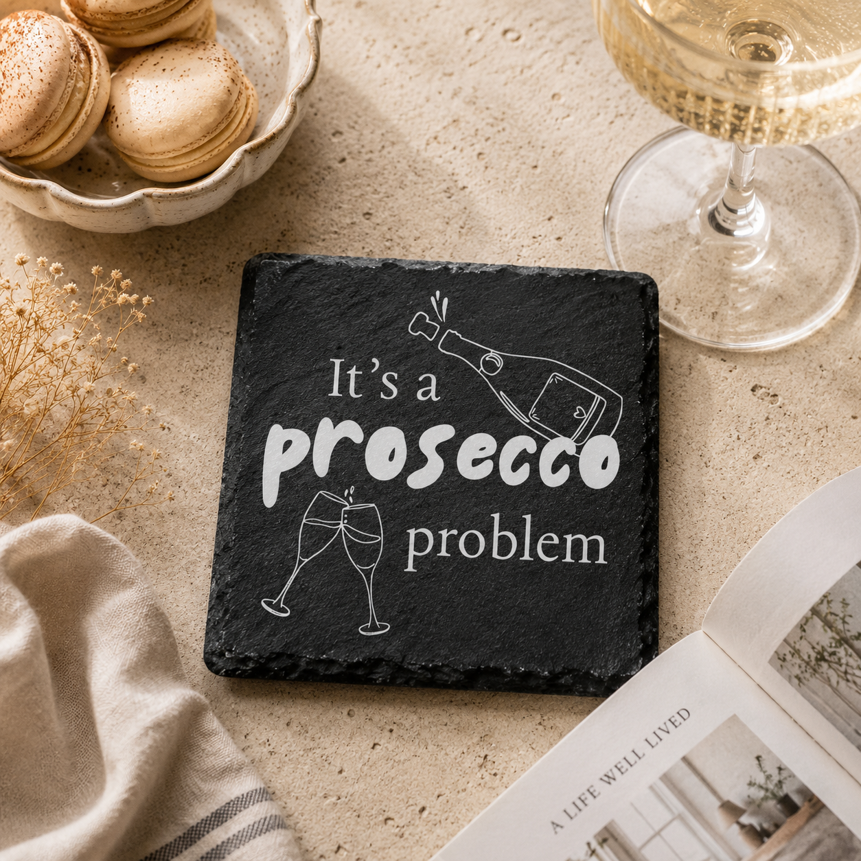 Slate coaster with 'It's a prosecco problem' text on a table with macarons and a glass of prosecco.