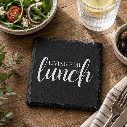 Slate coaster with 'Living for lunch' text on a wooden table with salad and water.